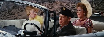 Movie still from “It's a Mad Mad Mad Mad World” (1963), directed by Stanley Kramer – A man and a woman sitting in the driver's seat of a car; Medium shot, Over the shoulder angle
