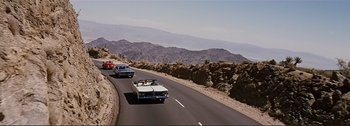 Movie still from “It's a Mad Mad Mad Mad World” (1963), directed by Stanley Kramer – A couple of cars driving down a road next to some mountains; Extreme Wide shot, High angle