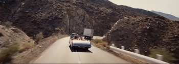 Movie still from “It's a Mad Mad Mad Mad World” (1963), directed by Stanley Kramer – A car driving down a road next to a rock wall; Extreme Wide shot, High angle