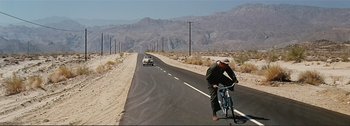 Movie still from “It's a Mad Mad Mad Mad World” (1963), directed by Stanley Kramer – A man riding a bike down the side of a road; Extreme Wide shot, High angle