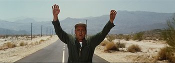 Movie still from “It's a Mad Mad Mad Mad World” (1963), directed by Stanley Kramer – A man standing on the side of a road with his hands up; Medium shot, Low angle