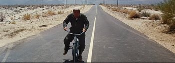 Movie still from “It's a Mad Mad Mad Mad World” (1963), directed by Stanley Kramer – A man riding a bike down a street; Wide shot, High angle