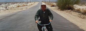 Movie still from “It's a Mad Mad Mad Mad World” (1963), directed by Stanley Kramer – A man riding a bike down a street; Wide shot, Low angle