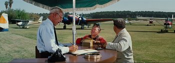 Movie still from “It's a Mad Mad Mad Mad World” (1963), directed by Stanley Kramer – Three men sitting at a table under an awning; Medium shot, Over the shoulder angle