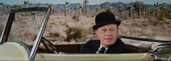 Movie still from “It's a Mad Mad Mad Mad World” (1963), directed by Stanley Kramer – An older man in a suit and hat driving a car; Close Up shot, Over the shoulder angle