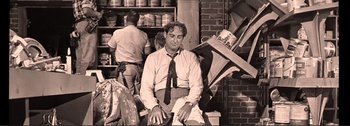 Movie still from “It's a Mad Mad Mad Mad World” (1963), directed by Stanley Kramer – A black and white photo of a man sitting in a store; Medium shot, Low angle
