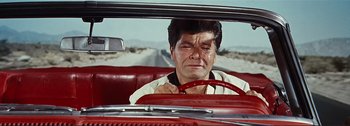Movie still from “It's a Mad Mad Mad Mad World” (1963), directed by Stanley Kramer – A man sitting in the driver's seat of a red car; Medium shot, High angle