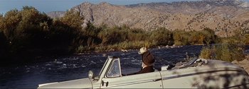 Movie still from “It's a Mad Mad Mad Mad World” (1963), directed by Stanley Kramer – A man wearing a cowboy hat driving a boat down a river; Wide shot, High angle