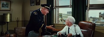 Movie still from “It's a Mad Mad Mad Mad World” (1963), directed by Stanley Kramer – A police officer talking to an older man in front of a window; Medium shot, Over the shoulder angle