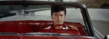Movie still from “It's a Mad Mad Mad Mad World” (1963), directed by Stanley Kramer – A man sitting in the driver's seat of a red car; Close Up shot, Low angle