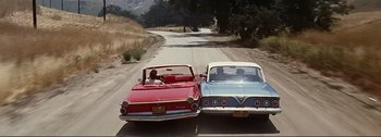 Movie still from “It's a Mad Mad Mad Mad World” (1963), directed by Stanley Kramer – A couple of cars parked next to each other on a road; Wide shot, High angle