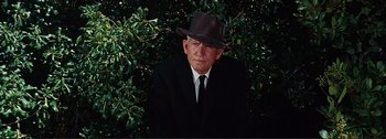 Movie still from “It's a Mad Mad Mad Mad World” (1963), directed by Stanley Kramer – An old man wearing a suit and a hat in front of a bush; Medium shot, Low angle