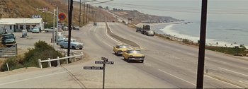 Movie still from “It's a Mad Mad Mad Mad World” (1963), directed by Stanley Kramer – A couple of cars driving down a road next to the ocean; Extreme Wide shot, High angle