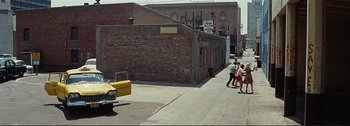 Movie still from “It's a Mad Mad Mad Mad World” (1963), directed by Stanley Kramer – Two people walking down the street in front of a brick building; Extreme Wide shot, High angle