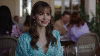 Movie still from “Emily in Paris” (2020), created by Darren Star – A woman in a polka dot dress sitting in front of a group of diners; Close Up shot, Over the shoulder angle