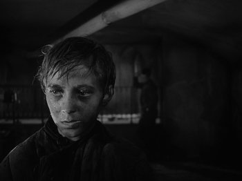 Movie still from “Ivan's Childhood” (1962), directed by Eduard Abalov – A young boy with dirty face and eyes stares into the camera; Close Up shot, Low angle