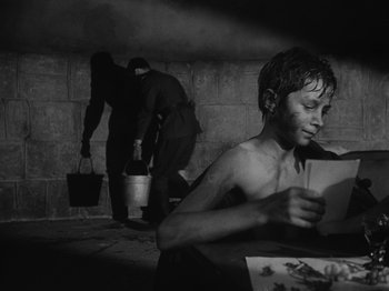 Movie still from “Ivan's Childhood” (1962), directed by Eduard Abalov – A young boy sitting at a table in a room; Medium shot, High angle