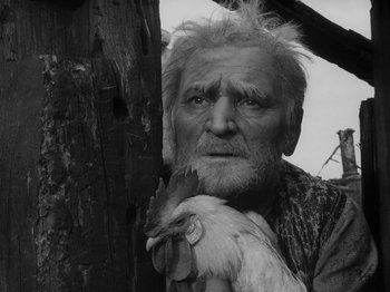 Movie still from “Ivan's Childhood” (1962), directed by Eduard Abalov – An old man holding a chicken in front of a wooden fence; Close Up shot, Low angle