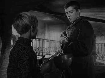 Movie still from “Ivan's Childhood” (1962), directed by Eduard Abalov – A young man is holding a bowl and talking to a young boy; Medium shot, Low angle