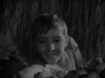 Movie still from “Ivan's Childhood” (1962), directed by Eduard Abalov – A young boy in the rain smiling at the camera; Close Up shot, High angle
