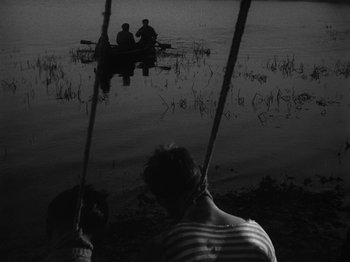 Movie still from “Ivan's Childhood” (1962), directed by Eduard Abalov – Three people in a boat on a body of water at night; Wide shot, High angle