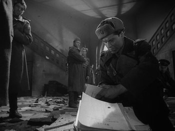 Movie still from “Ivan's Childhood” (1962), directed by Eduard Abalov – An old photo of a man looking at papers on the floor; Medium shot, High angle