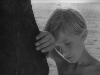 Movie still from “Ivan's Childhood” (1962), directed by Eduard Abalov – A young boy leaning against a tree in a black and white photo; Close Up shot, High angle
