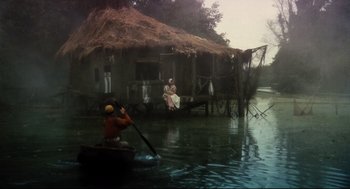 Movie still from “Jabberwocky” (1977), directed by Terry Gilliam – A man rowing a boat in front of a house; Extreme Wide shot, High angle