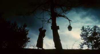 Movie still from “Jabberwocky” (1977), directed by Terry Gilliam – A person hanging from a tree with a basket hanging from a tree; Wide shot, Low angle