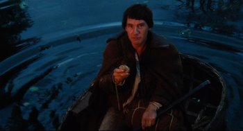 Movie still from “Jabberwocky” (1977), directed by Terry Gilliam – A man sitting in a boat holding a piece of food; Medium shot, High angle