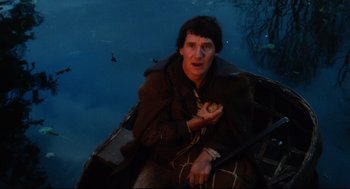 Movie still from “Jabberwocky” (1977), directed by Terry Gilliam – A man sitting in a boat holding a piece of food; Medium shot, High angle