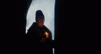 Movie still from “Jabberwocky” (1977), directed by Terry Gilliam – A person holding a candle in a dark room; Medium shot, Low angle