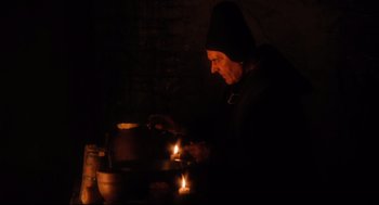 Movie still from “Jabberwocky” (1977), directed by Terry Gilliam – An old woman lighting candles in a dark room; Medium shot, High angle