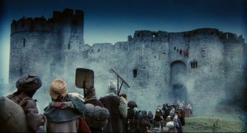 Movie still from “Jabberwocky” (1977), directed by Terry Gilliam – A group of people standing in front of an old castle; Extreme Wide shot, Low angle