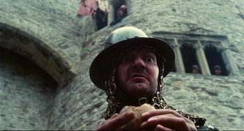 Movie still from “Jabberwocky” (1977), directed by Terry Gilliam – A man wearing chains and a helmet holding a piece of bread; Close Up shot, Low angle