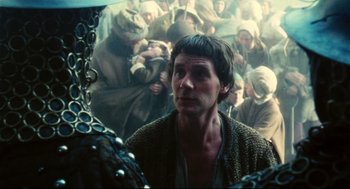 Movie still from “Jabberwocky” (1977), directed by Terry Gilliam – A man standing in front of a group of people; Close Up shot, Over the shoulder angle