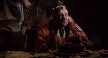 Movie still from “Jabberwocky” (1977), directed by Terry Gilliam – A man wearing a crown sitting in front of a table; Medium shot, Low angle