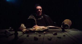 Movie still from “Jabberwocky” (1977), directed by Terry Gilliam – A man sitting at a table with a plate of food on top of it; Medium shot, High angle