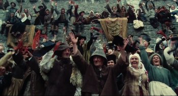 Movie still from “Jabberwocky” (1977), directed by Terry Gilliam – A group of people standing next to each other waving hands; Wide shot, Low angle