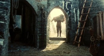 Movie still from “Jabberwocky” (1977), directed by Terry Gilliam – A man carrying a bag of hay through an archway; Wide shot, Low angle