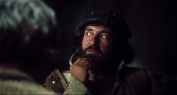 Movie still from “Jabberwocky” (1977), directed by Terry Gilliam – A man with a beard wearing a hat and looking up; Close Up shot, Over the shoulder angle