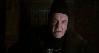 Movie still from “Jabberwocky” (1977), directed by Terry Gilliam – An old man wearing a black hat and a black robe; Close Up shot, Low angle