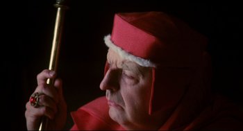 Movie still from “Jabberwocky” (1977), directed by Terry Gilliam – An older woman wearing a red hat and holding a pipe; Close Up shot, High angle