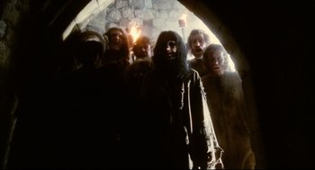 Movie still from “Jabberwocky” (1977), directed by Terry Gilliam – A group of people standing in front of an archway with torches; Medium shot, Low angle