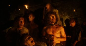 Movie still from “Jabberwocky” (1977), directed by Terry Gilliam – A group of men in a cave with a fire in the background; Medium shot, High angle