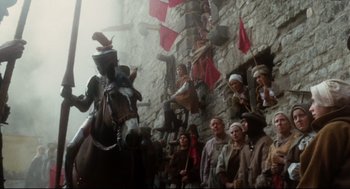 Movie still from “Jabberwocky” (1977), directed by Terry Gilliam – A man riding a horse in front of a group of people; Wide shot, Low angle