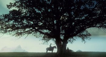 Movie still from “Jabberwocky” (1977), directed by Terry Gilliam – A person on a horse under a large tree; Extreme Wide shot, Low angle