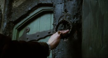 Movie still from “Jabberwocky” (1977), directed by Terry Gilliam – A hand is touching a door knob on a wooden door; Extreme Close Up shot, High angle