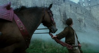 Movie still from “Jabberwocky” (1977), directed by Terry Gilliam – A man leading a brown horse through a grassy field; Wide shot, Low angle