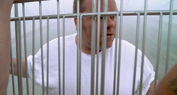 Movie still from “Jackass: The Movie” (2002), directed by Jeff Tremaine – A man in white shirt behind a metal fence; Close Up shot, Overhead angle